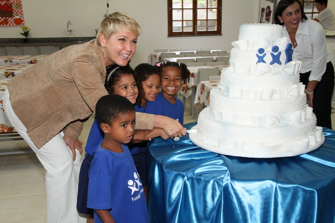 Xuxa ajuda as crianças envolvidas no projeto a cortar o bolo