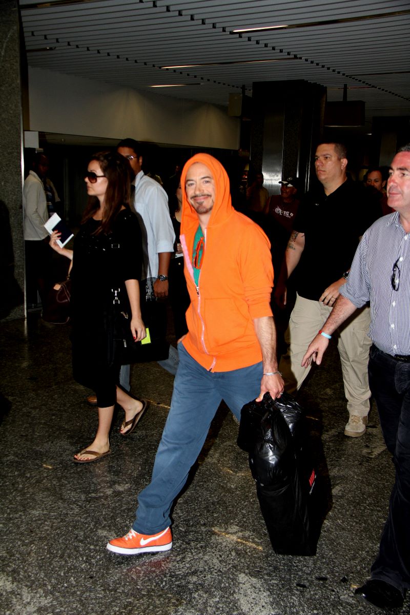 Robert Downey Jr. caminha pelo saguão do aeroporto do Rio com um sorrisão no rosto
