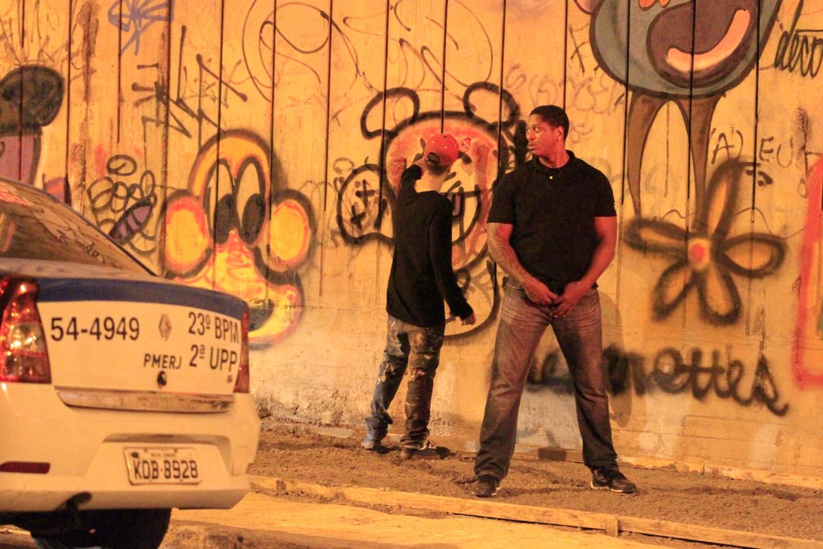 Justin Bieber faz desenho no muro, enquanto é protegido por um segurança, em São Conrado, no Rio
