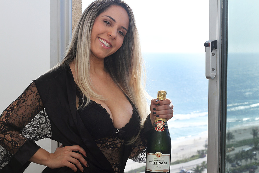 Mulher Melão posa de camisola chique em frente à janela de seu novo apartamento na Barra da Tijuca: champanhe para comemorar