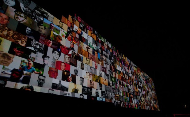 Centenas de pessoas mortas em conflitos têm suas imagens exibidas nos tijolos do gigantesco muro erguido durante o show (Foto: Flavio Morais/G1)