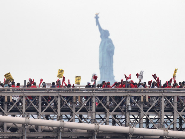 Com a Estátua da Liberdade ao fundo, grupos pró-imigrantes marcham pela Ponte do Brooklyn, em Nova York, nesta quinta-feira (29). Eles pedem a derrubada total da nova lei de imigração do Arizona, argumentando que ela alimenta um clima racista no país. Uma