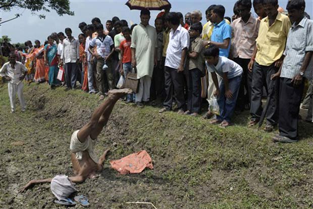 Multidão observa indiano com a cabeça enterrado no chão.