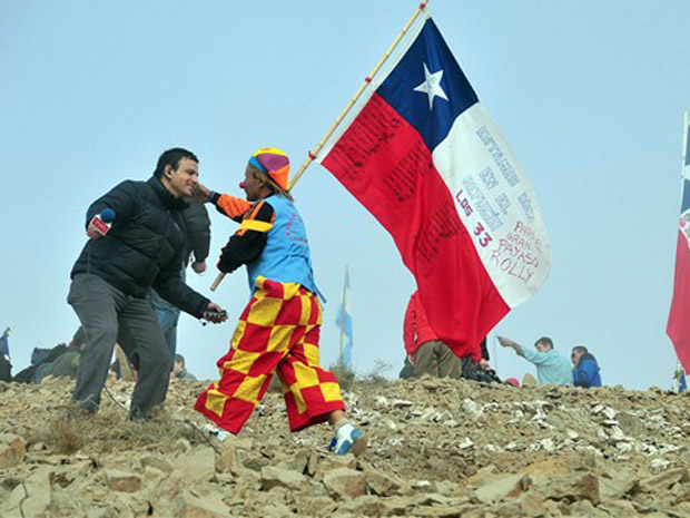 Repórter de TV e homem vestido de palhaço, com bandeira do Chile, comemoram a abertura do túnel.