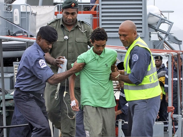 Um dos naufragos é ajudado ao chegar à base naval de Stanley Brown, em Suva, Fiji