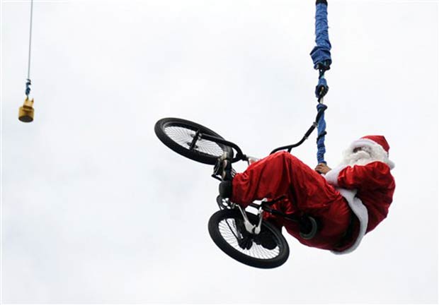 Vestido de Papai Noel, homem pula com bicicleta de bungee jump, na quinta-feira, em praia em  Kuta, na Indonésia.