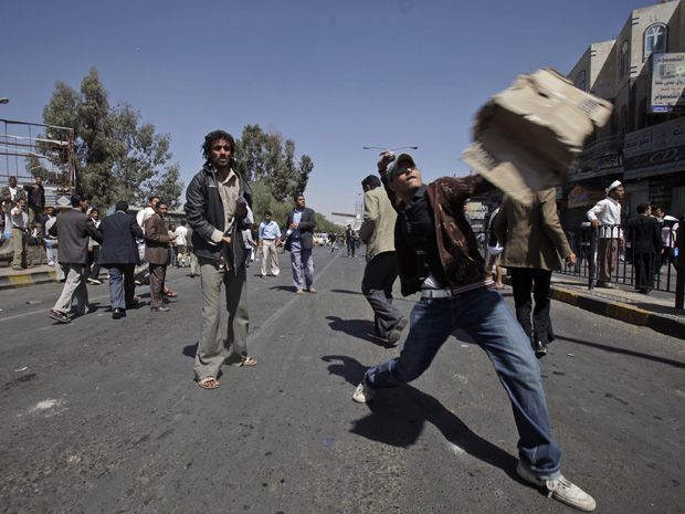 Um manifestante anti-governo atira uma pedra na direção de defensores do governo do Iêmen durante conflito em Sanaa, neste sábado (19). A repressão a protestos antigoverno no Iêmen provocaram mais mortes no Iêmen, onde manifestantes protagonizam protestos (Foto: AP)