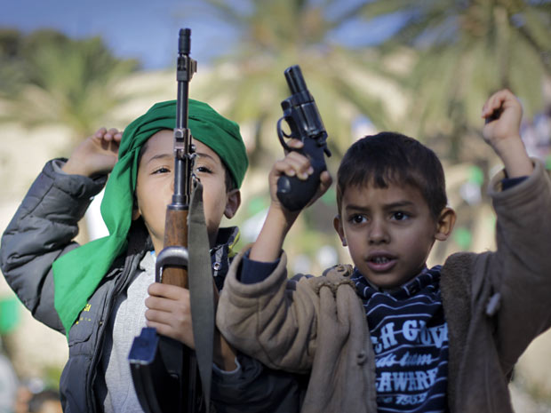 Filhos de um soldado pró-Kadhafi seguram armas do pai em manifestação a favor do ditador líbio, em Trípoli (Foto: Ben Curtis/AP)