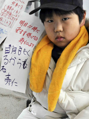 Toshihiko Aisawa, de 9 anos, percorre abrigos com placas com nome dos pais, da avó e dos primos, que foram levados pelo tsunami (Foto: Kuniaki Nishio/AP)