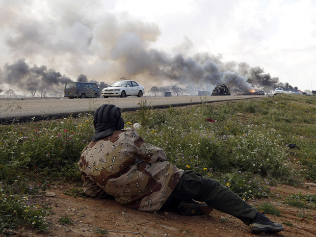 Rebelde líbio observa veículos das forças pró-Kadhafi queimando após ataque aéreo da coalizão, na estrada entre Benghazi e Ajdabiyah, neste domingo (20). (Foto: Reuters)