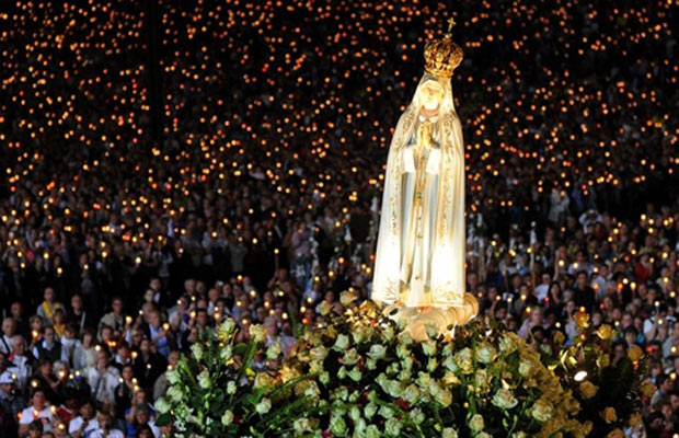 Fiéis carregam imagem de Nossa Senhora de Fátima em procissão em Fátima, Portugal, na noite desta quinta-feira (12). Centenas de peregrinos celebraram o aniversário do milagre de Fátima, em que três crianças pastora afirmaram ter visto a virgem, em 1917. (Foto: AFP)