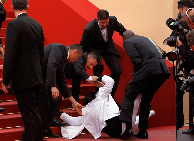 Vestido com um terno branco, o invasor foi imobilizado por outros seguranças depois de cair das escadas (Foto: AP)