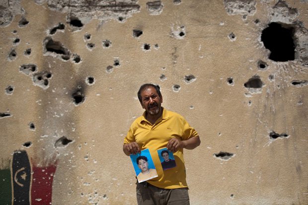 Em frente a parede com buracos de tiros em Misrata, homem mostra fotos de dois filhos desaparecidos há dois meses, segundo ele levados por forças ligadas a Muammar Kadhafi. (Foto: AP)