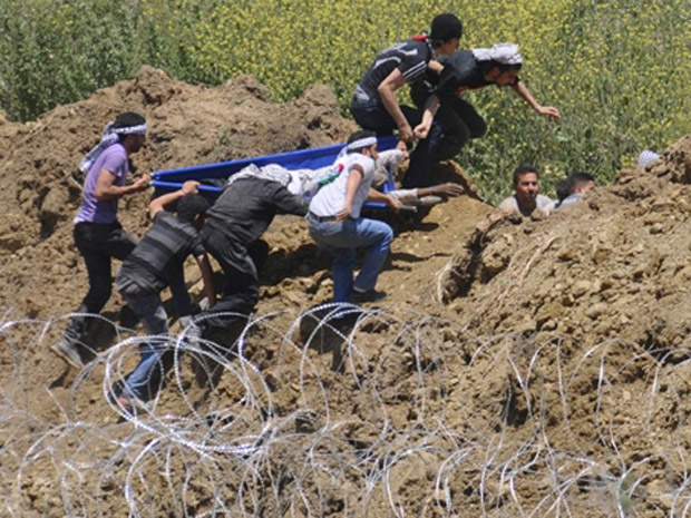 Palestinos carregam manifestante ferido pelo ataque israelense neste domingo (5) nas colinas de Golan (Foto: AFP)