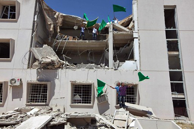 Líbios carregam bandeiras nos escombros de uma universidade em Trípoli, em 18 junho de 2011. Autoridades informaram que prédio foi atingido no dia anterior por ataques aéreos da Otan (Foto: AFP)