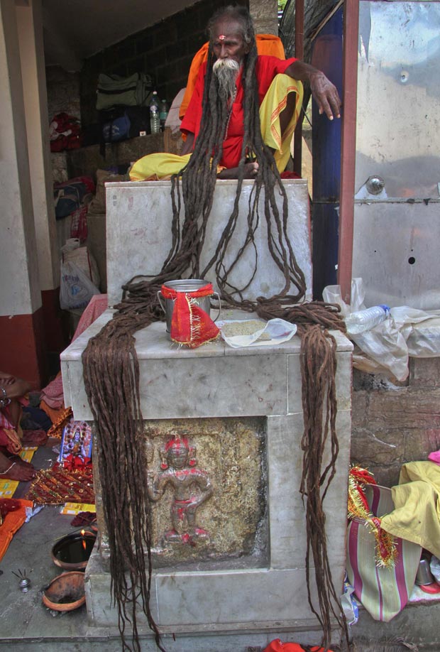 Homem estendeu os longos dreads em volta de um pote onde as doações podem ser colocadas. Ele é um "sadhu", considerado um homem santo na religião hindu (Foto: Utpal Baruah/Reuters)