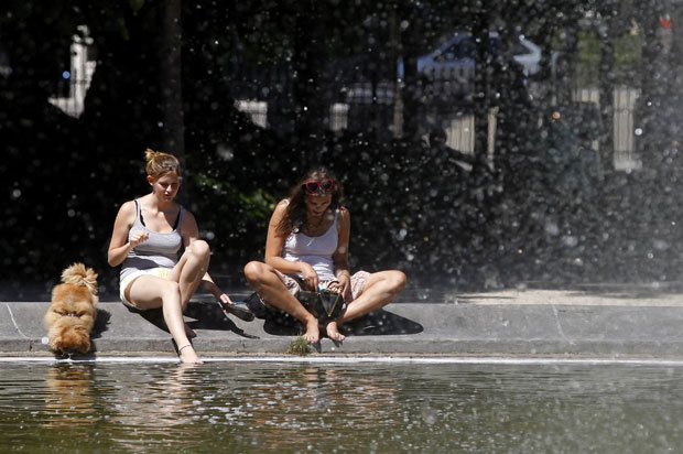 Mulheres e um cachorro se refrescam à beira de uma fonte em Bruxelas, na Bélgica, que teve temperaturas acima dos 30° centígrados (Foto: Reuters)