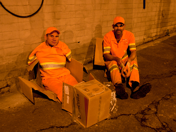 Os coletores de lixo José Ubirajara e Elias Celestino entram em caixas de papelão para se esquentar enquanto aguardam o caminhão de lixo buscá-los. (Foto: Daigo Oliva/G1)
