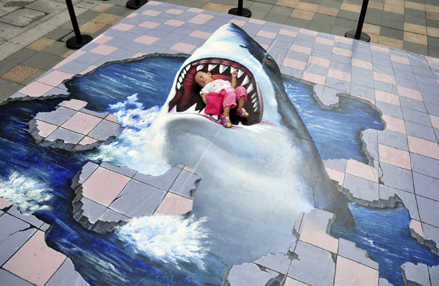 Um casal chinês teve uma ideia de foto engraçada e colocou a pequena filha sobre uma pintura em 3D de um tubarão, exposta no chão de um shopping center em Fuzhou, na província de Fujian. A impressão é de que a menina está sendo engolida pelo animal. (Foto: Reuters/China Deily)