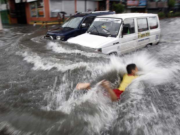 Um menino nada em água de enchente enquanto carros tentam avançar por uma rua de Manila. (Foto: Romeo Ranoco / Reuters)