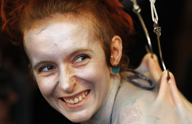 A artista performática britânica Alice Newstead sorri nesta quarta-feira (24) ao ser suspensa pelas costas por ganchos em uma loja de cosméticos em San Francisco, no estado americano da Califórnia (Foto: Reuters)