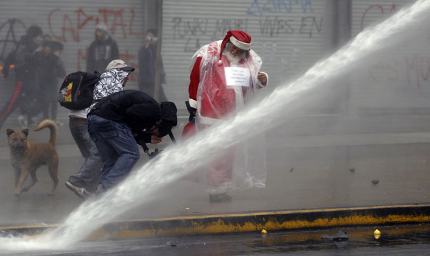 Homem vestido de Papai Noel participa dos protestos enquanto polícia usa jato d'água para conter manifestantes (Foto: AP)