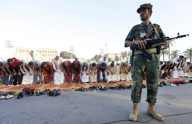 Rebelde líbio faz a guarda enquanto fiéis rezam na Praça Verde de Trípoli (Foto: Isamil Zitouny/Reuters)