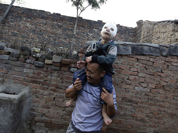 Pai brinca com Wang Gengxiang, o 'Menino Mascarado' (Foto: Jason Lee / Reuters)