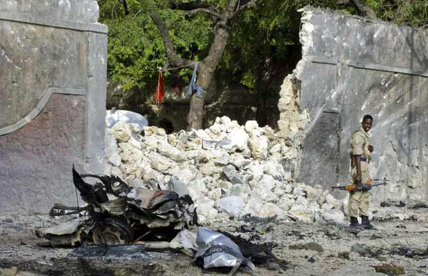 Soldado somali ao lado dos restos do carro-bomba que explodiu nesta terça-feira (18) em Mogadício (Foto: AP)
