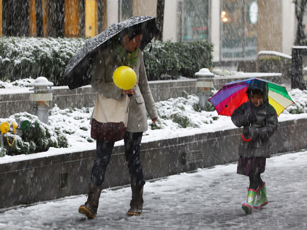 Uma mulher e uma criança usam guarda-chuvas para se protegerem da neve que cai  (Foto: Reuters)