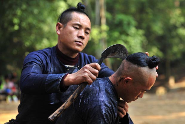 Homem usa foice para raspar o cabelo de outro morador. (Foto: Sheng Li/Reuters)