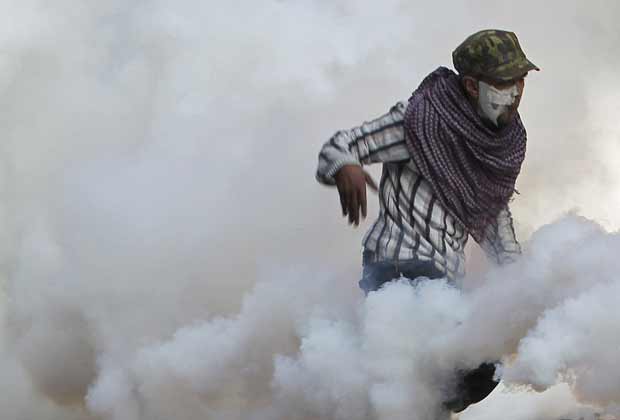 Manifestante devolve granada de gás jogada pela polícia durante confronto próximo à Praça Tahrir, no Cairo, nesta quarta-feira (23) (Foto: AP)