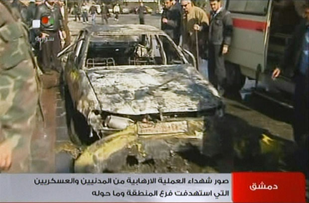 Sírios inspecionam a carcaça de um carro queimado no local de uma explosão (Foto: AFP/TV síria)