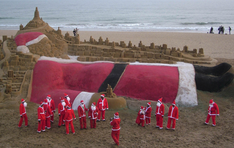 Artistas vestidos como papai noel criam uma escultura de areia durante a celebração do Natal na praia de Puri, na Índia, neste sábado (24)
