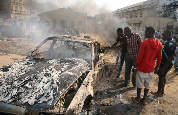 Homens olham para dentro de um carro que explodiu próximo a uma igreja católica em Abuja, capital da Nigéria, neste domingo (25) (Foto: AFP)