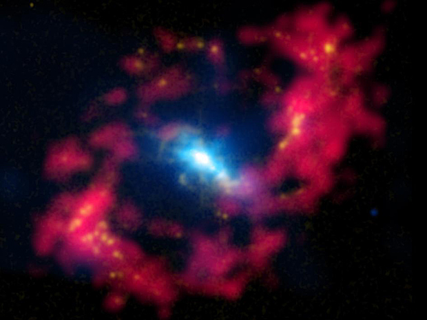 Anel de fogo (Foto: Um “anel de fogo” captado pelo telescópio de raio-X Chandra, da agência espacial americana (Nasa), e divulgado nesta terça-feira (27) mostra a região central da galáxia espiral NGC 4151, localizada a 43 milhões anos-luz de distância da Terra e uma das mais próximas a ter um buraco negro ativo. Informações de raio-X (em azul) foram combinadas com dados óticos (em amarelo), e as bolhas amarelas em volta da elipse vermelha são regiões de formação estelar recente. Já o anel vermelho contém uma mistura de hidrogênio com um material que cai em direção ao centro da galáxia. Foto: X-ray: NASA/CXC/CfA/J.Wang et al.; Optical: Isaa)