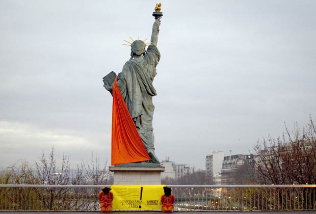 Réplica parisiense da Estátua da Liberdade é coberta com lona nesta terça-feira (10); ao pé da escultura, ativistas se vestem como prisioneiros (Foto: AFP)