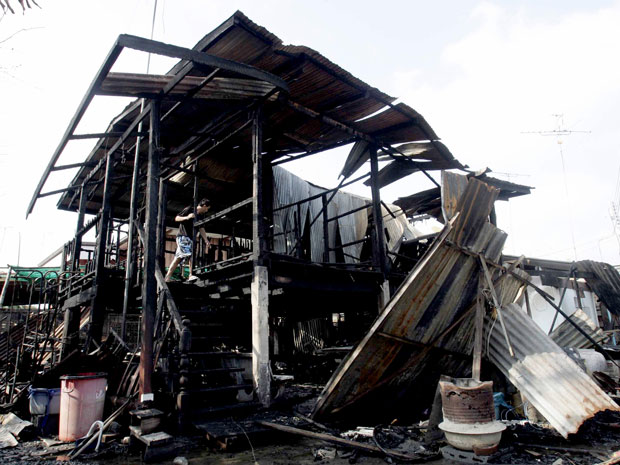 Um morador tailandês verifica o que sobrou de sua casa, que também foi incendiada por fogos de artifício na província de Suphanburi, ao norte de Bangcoc (Foto: AP Photo)