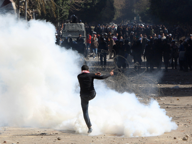 Manifestante egípcio chuta bomba de gás lacrimogênio durante confrontos com a polícia, no Cairo (Foto: AFP)