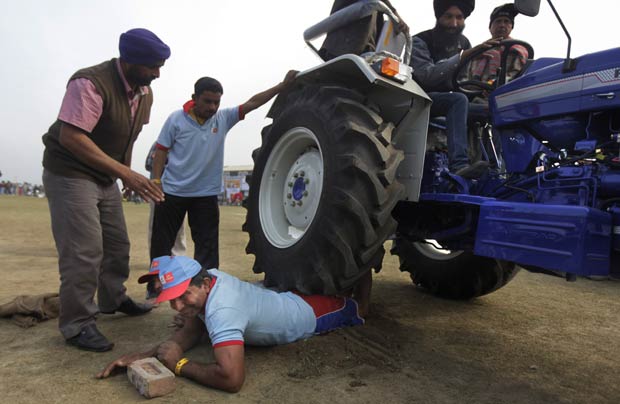 Homem se deixa atropelar por trator com três pessoas durante festival rural em Kila Raipur, próximo à cidade indiana de Ludhiana. A demonstração de força é parte do festival esportivo conhecido como 'Olimpíadas Rurais da Índia' (Foto: Altaf Qadri/AP)