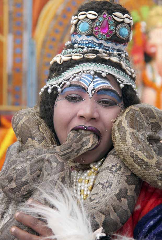Garoto caracterizado como o deus hinduísta Shiva morte a cabeça de serpente em parque próximo a templo em Chandigardh, na Índia (Foto: Ajay Verma/Reuters)