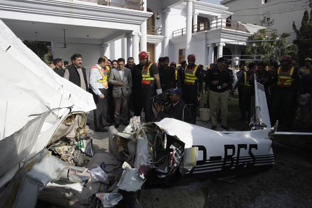 Moradores cercam destroços de avião de treinamento que caiu em área urbana da cidade de Lahore, no Paquistão, nesta quinta-feira (23). O acidente matou uma instrutora de voo, Anita Qureshi, e um piloto em treinamento, Waqar Asif, segundo a polícia. Ninguém ficou ferido em solo no bairro de Model, um dos mais ricos da cidade (Foto: AP)