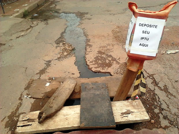 Moradores colocam placa improvisada em buraco cobrando IPTU. (Foto: Andréia de Souza / Arquivo Pessoal)