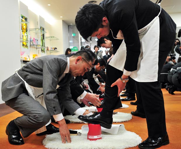 Funcionários ensinam jovens recém-contratados a engraxar o sapato. (Foto: Yoshikazu Tsuno/AFP)