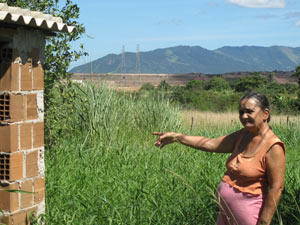 Ivanilda, ao lado de seu pequeno poço artesiano, aponta para o CTR, a cerca de dois quilômetros de distância (Foto: Lilian Quaino/G1)