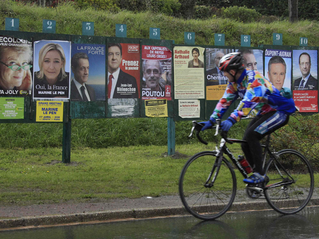 Ciclista passa em frente a painel com cartazes de candidatos à presidência da França,perto de Lille, neste sábado (21) (Foto: Reuters)
