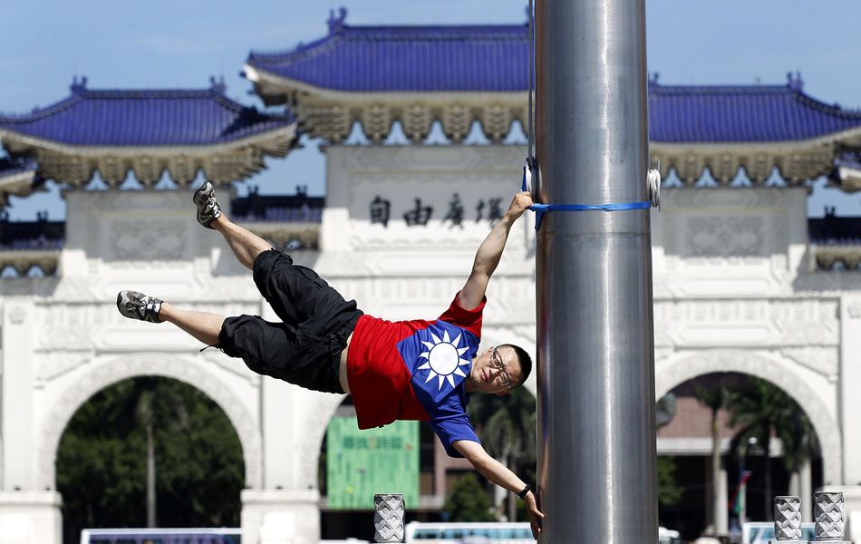 O ciclista Liao Hong-lin, de 29 anos, se apoia em um mastro em um ponto turístico de Taipei como se fosse uma bandeira enquanto veste uma camisa com as cores da bandeira de Taiwan...