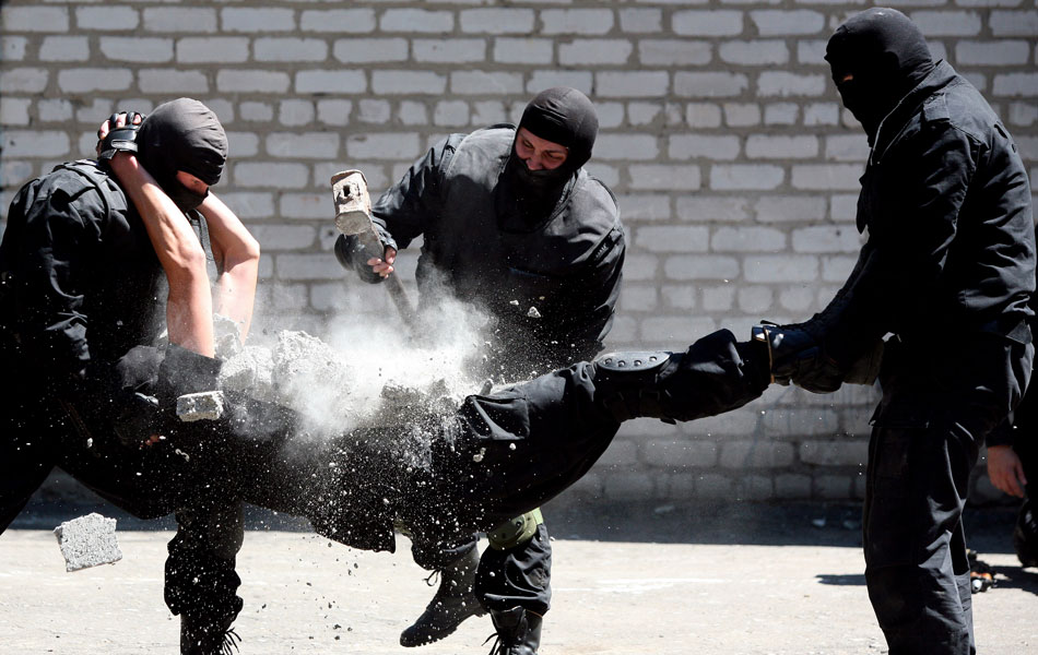 Policial ucraniano usa uma marreta para quebrar um pedaço de concreto sobre a barriga de um colega, apoiado por outros dois policiais, durante exibição de habilidades em treinamento numa área de Artyomovsk.