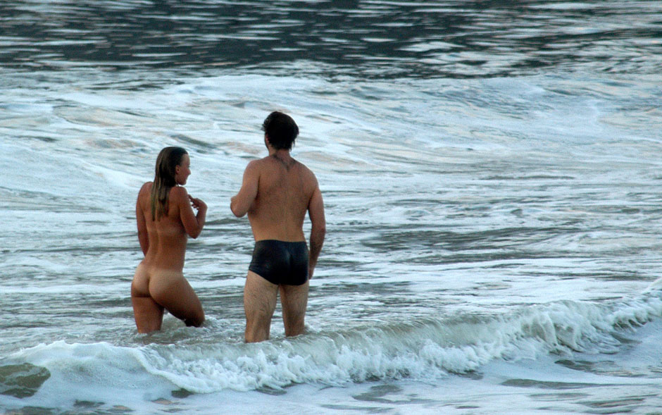 Turista toma banho nua na Orla do Flamengo, no Rio de Janeiro, durante o amanhecer. Pouco depois, ela saiu do mar e foi coberta com uma toalha pelo homem que a acompanhava.