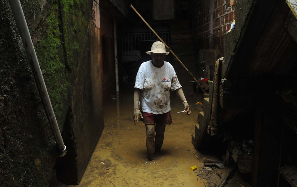Moradora anda na lama que invadiu a sua casa após a forte chuva que atingiu o bairro de Xerém, em Duque de Caxias, na Baixada Fluminense, nesta quinta-feira (3).